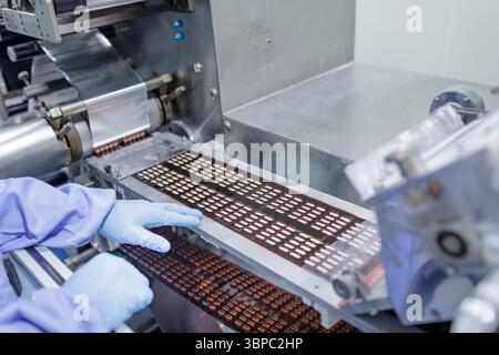 Automated blister packaging of tablets on a modern pharmaceutical production line with technician in sterile environment Stock Photo
