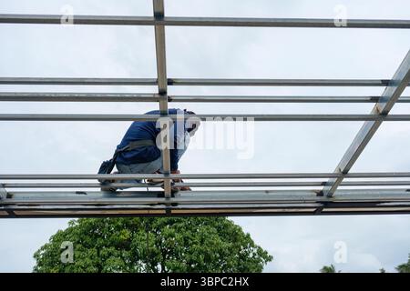 Construction worker installing and welding on steel frame of roof structure in construction site at outdoors Stock Photo