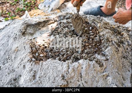 Construction worker manually mixes sand, cement, and water on the ground using a shovel and trowel, following a traditional outdoor concrete preparati Stock Photo