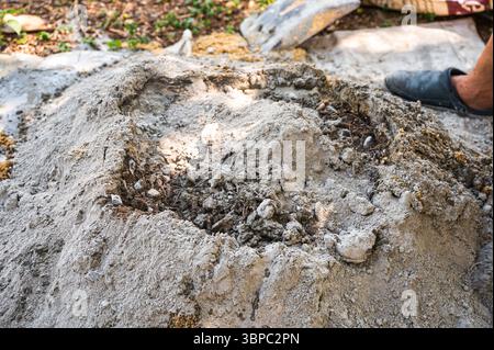 Construction worker manually mixes sand, cement, and water on the ground using a shovel and trowel, following a traditional outdoor concrete preparati Stock Photo