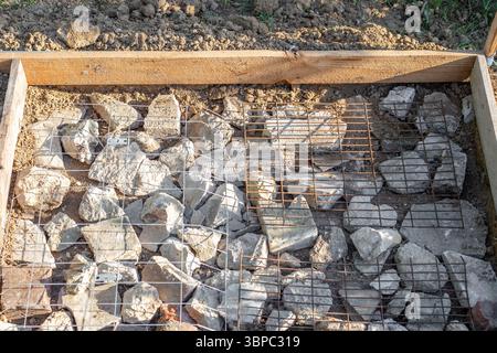 A construction site is prepared with rocks and wire mesh in a timber frame for pouring a concrete slab. Stock Photo