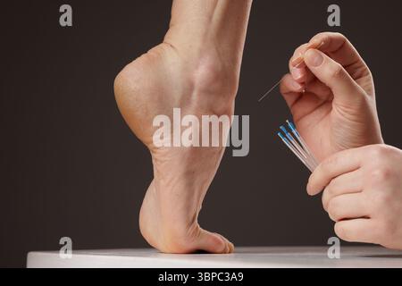 concept dry needling method, Acupuncture therapy on the foot, close-up of a practitioner's hands inserting thin needles into the heel for pain relief Stock Photo