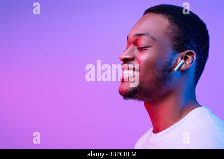 Relaxed African Man Listening Music In Wireless Airpods Earphones In Neon Light Stock Photo