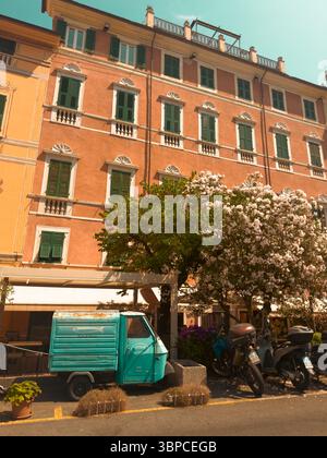 Street view in Italy of shutters shut on a building and a tiny three wheeled truck in front of a store front on a hot sunny summer day Stock Photo