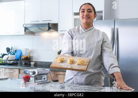 Female chef proudly showing fresh homemade tagliatelle pasta in a modern kitchen Stock Photo