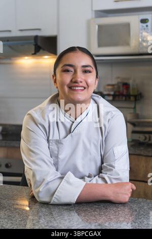 Portrait of a young smiling latin woman chef with arms crossed, posing in a professional kitchen Stock Photo