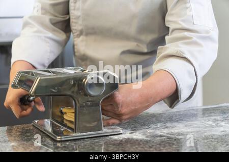Professional chef using a pasta maker to create fresh pasta in a restaurant kitchen Stock Photo