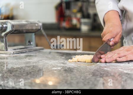 Professional chef preparing fresh pasta dough, cutting it into smaller pieces on a granite countertop in a commercial kitchen Stock Photo