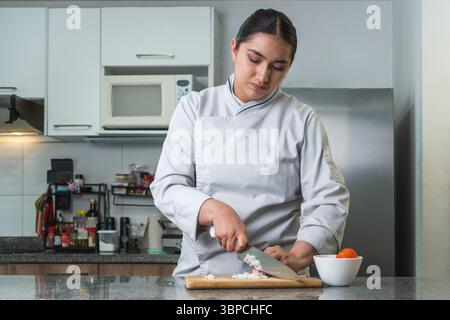 Concentrated female chef finely chopping onions on a wooden cutting board in a bright, modern kitchen setting Stock Photo