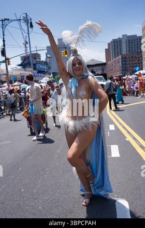 A woman in a feathered headdress and light blue cape participates in a street parade. She wears a white feathered costume and light-colored shoes.  Th Stock Photo