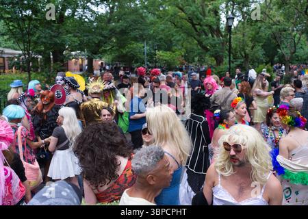 A large group of people, many in colorful attire and elaborate headwear, gather outdoors in a park-like setting.  The crowd is densely packed, with va Stock Photo