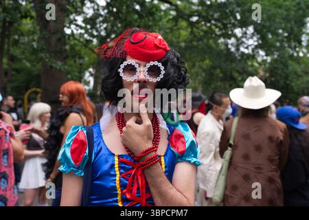 A person in a Snow White costume, wearing a red hat, daisy-shaped sunglasses, and red beaded necklaces, stands in a park with a thoughtful expression. Stock Photo