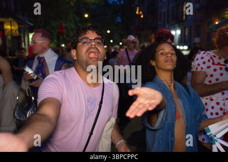 A man in a pink t-shirt with a floral design gestures towards the viewer, while a woman in a denim shirt looks towards the right side of the frame.  T Stock Photo