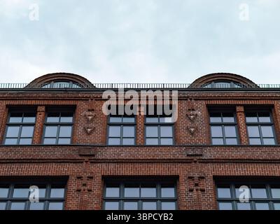 Old industrial building facade with a red clinker brick exterior. Symmetric architecture with large windows. Perspective from below with a cloudy sky. Stock Photo