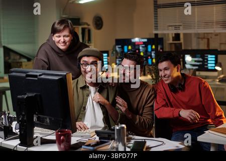 Group of multiethnic men and woman sitting at desk smiling and laughing while working together in scam call center office at night Stock Photo