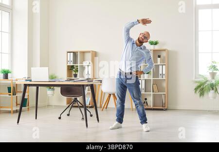 Young business man doing stretching sport exercises standing at the workplace in modern office. Stock Photo