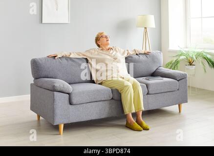 Senior relaxed woman wearing casual clothes sitting on comfortable sofa resting at home Stock Photo