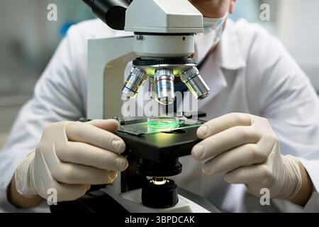 Scientist carefully places a chemical substance on a microscope slide, preparing to analyze it for the presence of pathogens. Focused on discovery Stock Photo