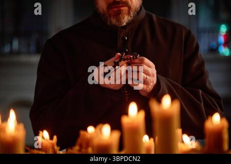 Middle Aged Caucasian Man Praying with Rosary Beads Surrounded by Candles Stock Photo