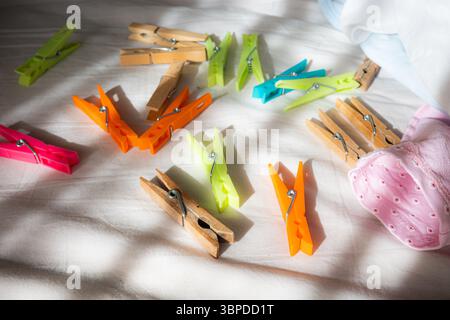 Colorful Clothespins Scattered on White Fabric with Sunlight and Shadows Stock Photo