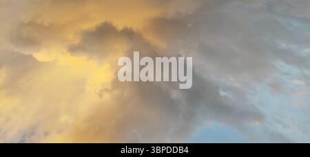 Dramatic evening sky with golden yellow and grey clouds illuminated by sunlight, captured in natural light just before sunset. Stock Photo