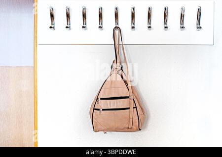 light leather backpack hanging on a hanger with metal hooks in a classroom, office. Back to school Stock Photo