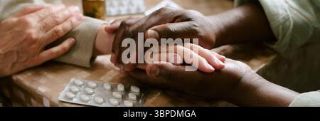 Senior Multiethnic Couple Comforting Each Other While Holding Hands at Table Stock Photo