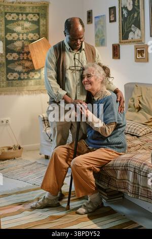 Senior Multiethnic Couple Embracing and Smiling Together in Modest Home Stock Photo