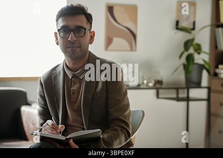 Portrait of Young South Asian Man Taking Notes during Therapy Session Stock Photo