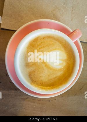 Coffee cup with latte art heart design sits on pink saucer and brown paper placemat Stock Photo