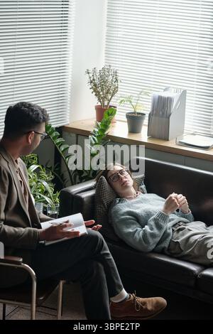 Young Woman Reclining on Sofa Sharing Thoughts with Therapist Stock Photo