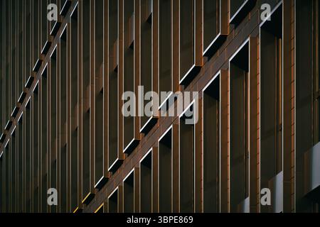 Modern building façade with repeating vertical windows lit by warm sunlight, creating strong geometric contrast and rhythm Stock Photo