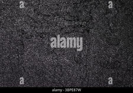 Close-up view of cracked black asphalt, showcasing its rough texture and providing a dark, gritty backdrop Stock Photo