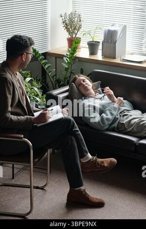 Young Woman Lying on Sofa Talking to Male Therapist during Session Stock Photo