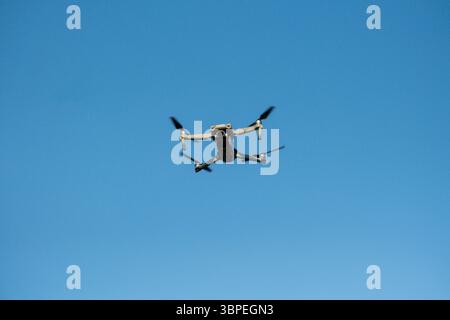 Flying Drone in Clear Blue Sky – Front View of Quadrocopter in Flight Stock Photo