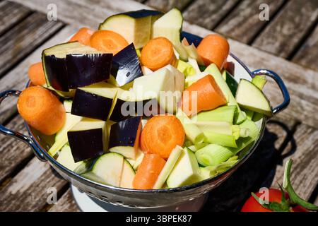 Vibrant carrots, zucchini, eggplant, and leeks sit in a colander, ready for preparation, on a rustic wooden table Stock Photo