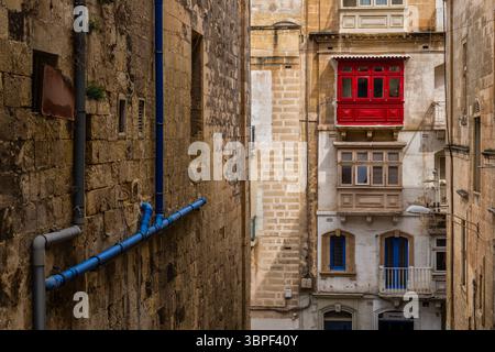 Urban architecture in old city of Valletta in Malta. Stone wall with external pipes and traditional Maltese houses with closed wooden balconies. Stock Photo