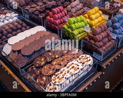 Colourful French macarons and artisan chocolates on display at a patisserie stall in the famous La Boqueria food market, Barcelona, Spain. Stock Photo