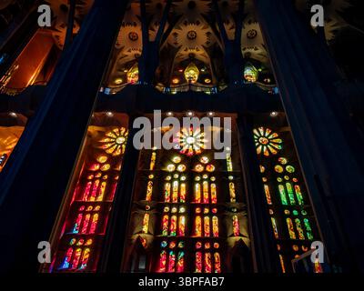 The warm red, orange, and yellow hues of the stained glass windows glowing in the dark interior of La Sagrada Familia basilica, Barcelona, Spain. Stock Photo