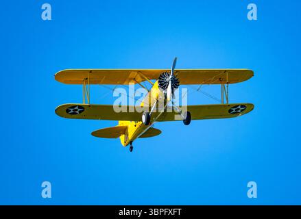 A bright yellow Boeing Stearman biplane flying in blue sky. California, USA. Stock Photo