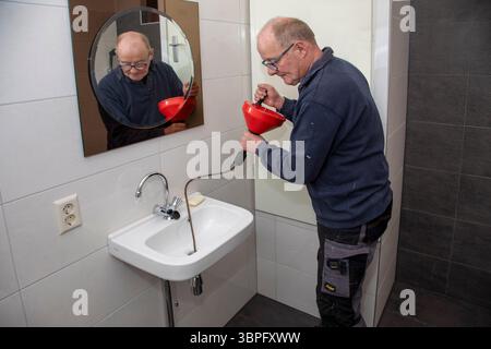 Netherlands, a plumber is using a handheld drain auger or 'plumber's snake'. Handheld drain augers are typically designed to clean portions of a drain Stock Photo