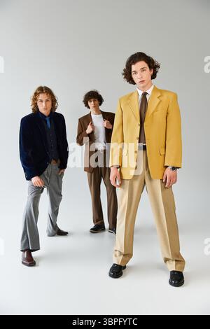 Three young men display their fashionable outfits in a contemporary studio, radiating confidence. Stock Photo