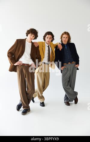 Three young men confidently display their unique styles and friendship against a simple backdrop. Stock Photo