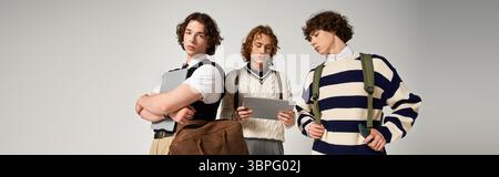 Three young men proudly display their fashion choices while carrying bags and electronics. Stock Photo