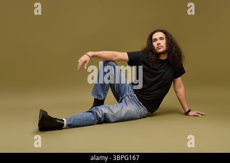 A young man in a black shirt and jeans poses confidently against a green background. Stock Photo