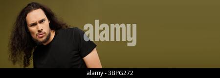A bearded young man stands confidently, playfully posing against a soft backdrop. Stock Photo