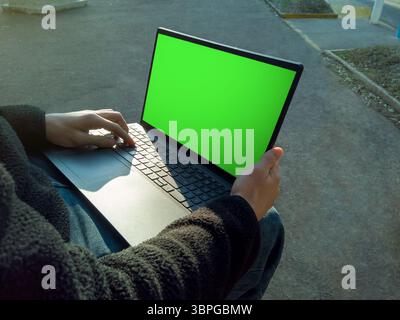 College student using laptop with green screen outdoors, working on school project on campus Stock Photo