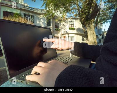 Student using laptop outdoors pointing at the screen with buildings and trees in the background Stock Photo