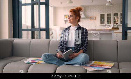 Smiling happy dreaming looking away thinking idea designer homeowner apartment house repair design colorful palette colors holding notebook smiling at Stock Photo