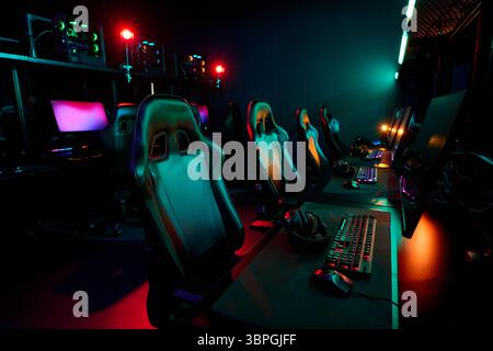 Empty gaming chairs and computer setups arranged in esports arena, illuminated by colorful lights, showing professional gaming environment prepared for girls gamers team competition Stock Photo
